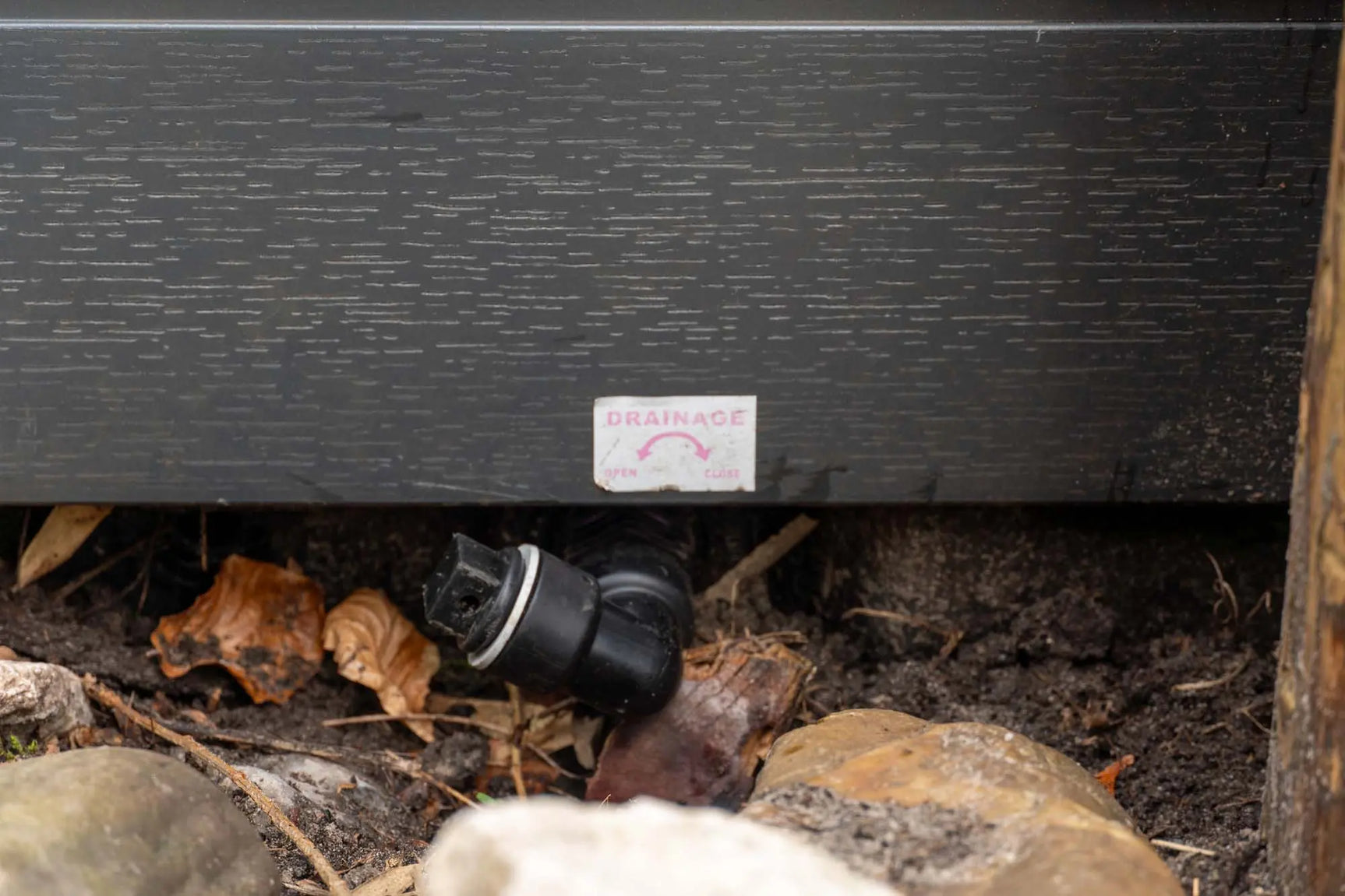Zwarte afvoerventiel voor jacuzzi buiten bij stenen en bladeren, geschikt voor swimspa of zwemspa.