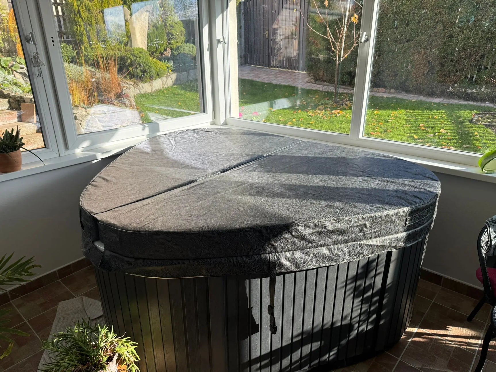 Zwarte 2-persoons jacuzzi met beschermhoes in lichte serre, ideaal als swimspa of jacuzzi buiten.