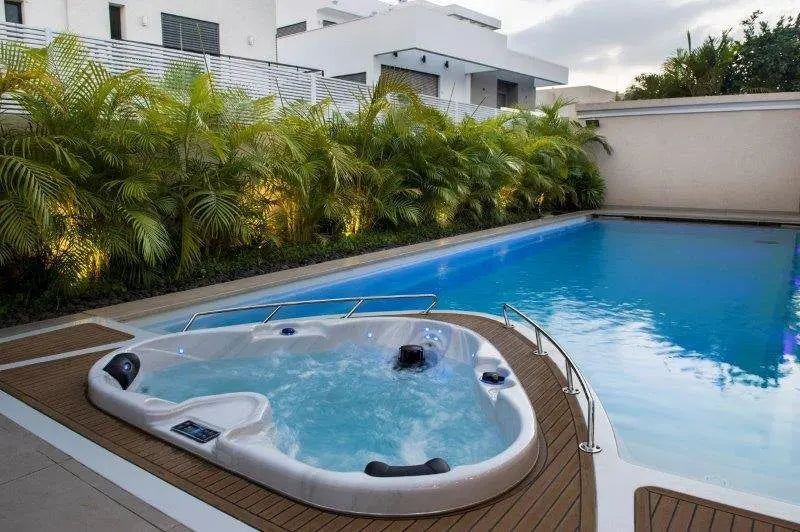 Witte 2-persoons jacuzzi buiten naast blauw zwembad op houten terras, ideale swimspa voor ontspanning.