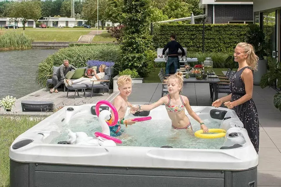 Ruime witte jacuzzi buiten met bubbeljets en kinderen die spelen in deze zwemspa swimspa.