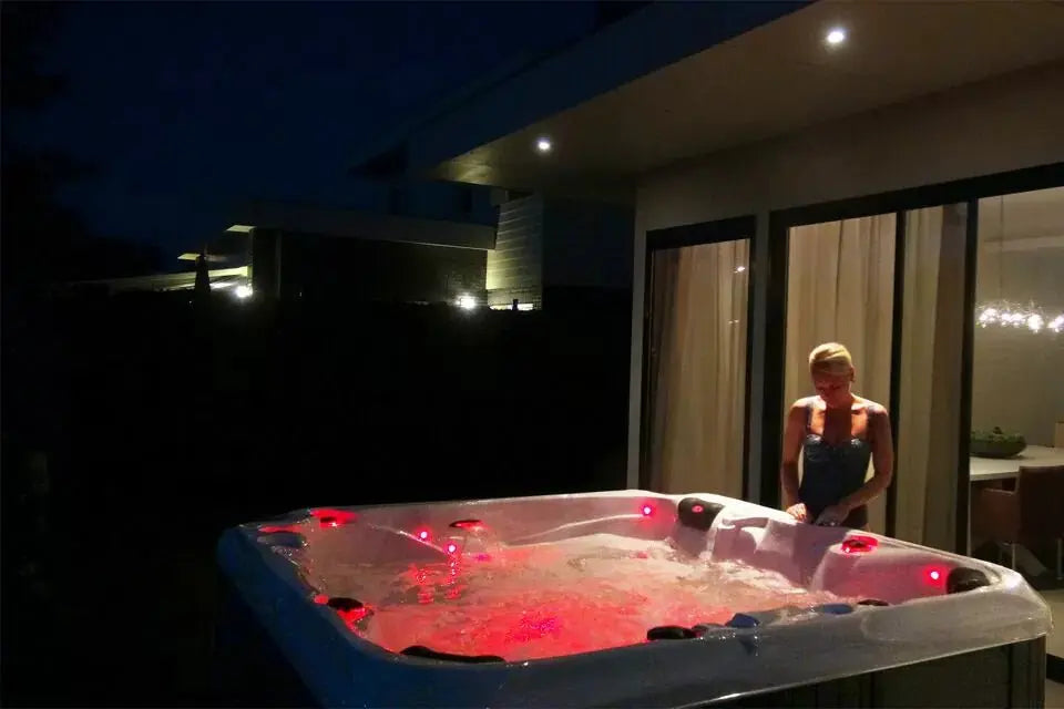 Moderne 6-persoons jacuzzi buiten met rode LED-verlichting, ideaal als swimspa en zwemspa voor ontspanning nachts.