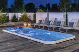 Illuminated Dynamic Deep swim spa on wooden deck with luxury loungers at dusk - Passion Spas Sport Collection