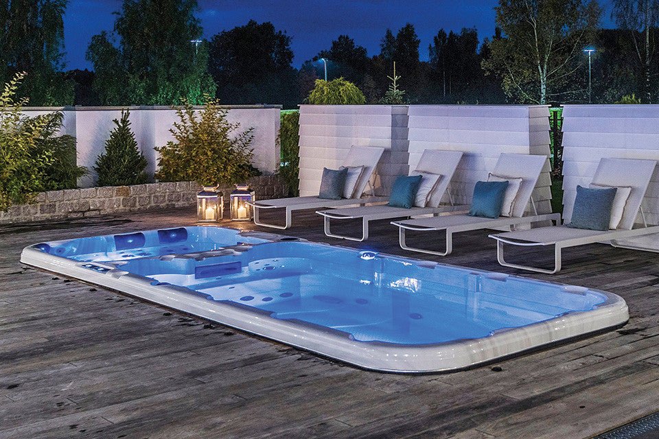 Illuminated Dynamic Deep swim spa on wooden deck with luxury loungers at dusk - Passion Spas Sport Collection