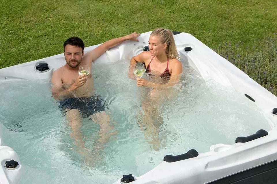 Two people enjoying drinks while relaxing in Desire luxury hot tub in outdoor garden setting - Passion Spas Signature Collection
