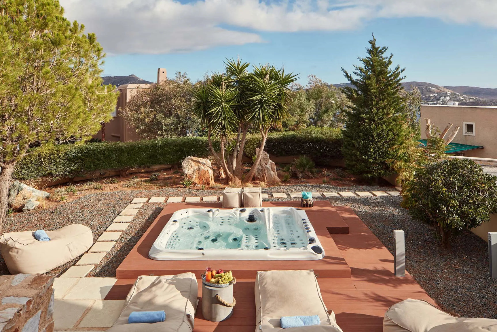 Witte jacuzzi buiten in tuin met houten terras en ligstoelen, perfecte swimspa voor 7 personen.