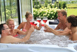 Friends enjoying drinks and relaxation in Felicity Wave Bench spa by garden, Passion Spas Exclusive Collection hot tub.