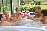 Vijfpersoons witte jacuzzi buiten met whirlpool jets en ontspannen mensen die toosten in swimspa.