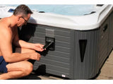 Person performing maintenance on Euphoria luxury hot tub with grey cabinet panel near patio - Passion Spas Exclusive Collection